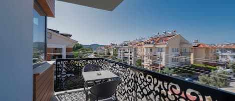 A balcony with a table and chairs, overlooking a residential area with multiple buildings and a clear sky.