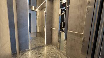 An elevator interior with metallic walls, a marble floor, and a control panel with buttons and a digital display.