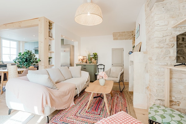A cozy living room with a sectional sofa, a coffee table, a patterned rug, and a stone wall.