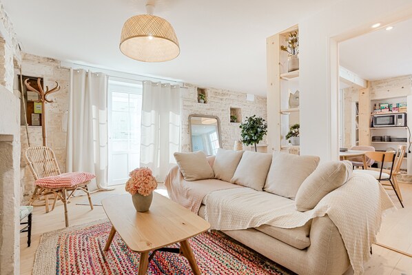 Una sala de estar acogedora con un sofá, una mesa de centro de madera, una silla de mimbre y una alfombra colorida.