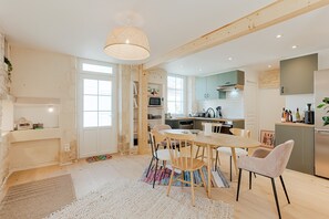 A modern kitchen with wooden beams, a dining area with a round table and chairs, and a large window.