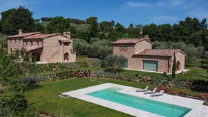 Una casa in pietra su due piani con piscina, immersa in giardini curati e alberi.