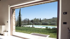 Vista da una stanza con una grande finestra che si affaccia su una piscina, un'area verdeggiante e alberi.