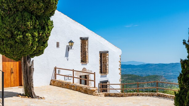 A white building with stone steps, a wooden door, and a railing overlooking a mountainous landscape. - La Rosa de los Vientos – Charming Stay with Sea Views for Peaceful Days (La Serratella)