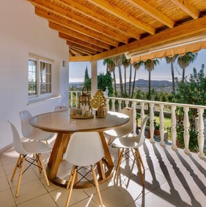 Un pati exterior cobert amb taula rodona i cadires, vista al paisatge i sostre de fusta.