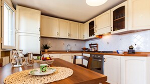 A kitchen with white cabinets, a wooden table with a placemat, a coffee maker, and a sink. - Apartment 'Anita' with Sea View, Private Terrace and Wi-Fi (Capoliveri)