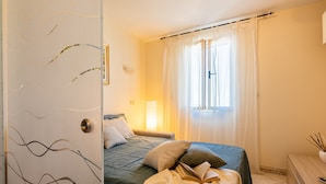 A bedroom with a bed, pillows, a bedside table, a lamp, and a window with curtains. - Apartment 'Anita' with Sea View, Private Terrace and Wi-Fi (Capoliveri)
