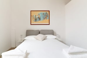 Un dormitorio con cama, almohadas, una mesita de noche y una obra de arte enmarcada en la pared.