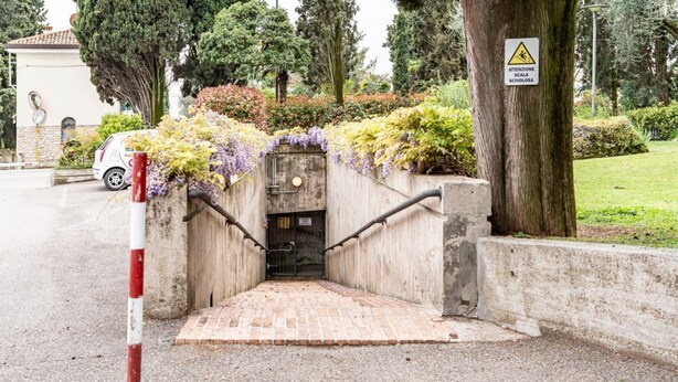 A gated entrance with a brick pathway leading to a building, surrounded by greenery and a warning sign.