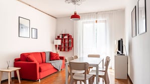A modern living room with a red sofa, a dining table with chairs, a white cabinet, and a TV.