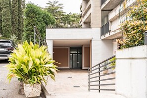 A building entrance with a gated driveway, a potted plant, and a staircase leading to a balcony.
