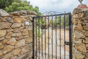 A stone wall with a metal gate, a stone pathway, and a building in the background.