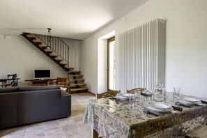 A dining area with a table set for four, a sofa, a staircase, and a radiator. - GuestHost - Charming independent farmhouse of about 100 sqm, perfect for 4 people, structured on two levels (second floor accessible by stairs).The property is a Rustico dating back to the 19th century, completely renovated, and is located in the heart o (Fossombrone)