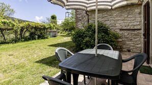 Une terrasse extérieure avec une table et des chaises, un parasol à rayures et un bâtiment en pierre en arrière-plan.