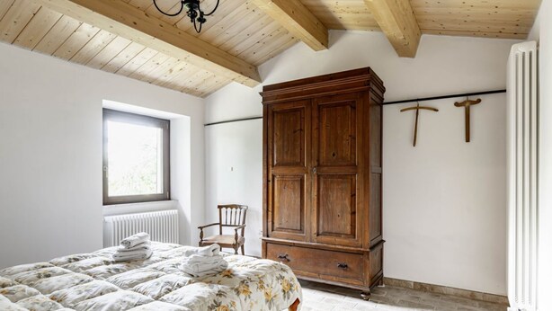 Une chambre à coucher comprenant un lit, une armoire en bois, un radiateur, une fenêtre et une chaise.