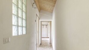 Un couloir étroit doté d’un sol carrelé, d’un plafond en bois et d’une grande fenêtre à vitre dépolie.