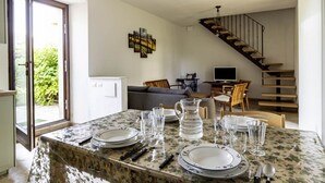 Un coin repas avec une table dressée pour quatre personnes, un escalier et un canapé en arrière-plan.