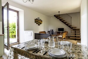A dining area with a table set for four, a staircase, and a sofa in the background. - GuestHost - Charming independent farmhouse of about 100 sqm, perfect for 4 people, structured on two levels (second floor accessible by stairs).The property is a Rustico dating back to the 19th century, completely renovated, and is located in the heart o (Fossombrone)