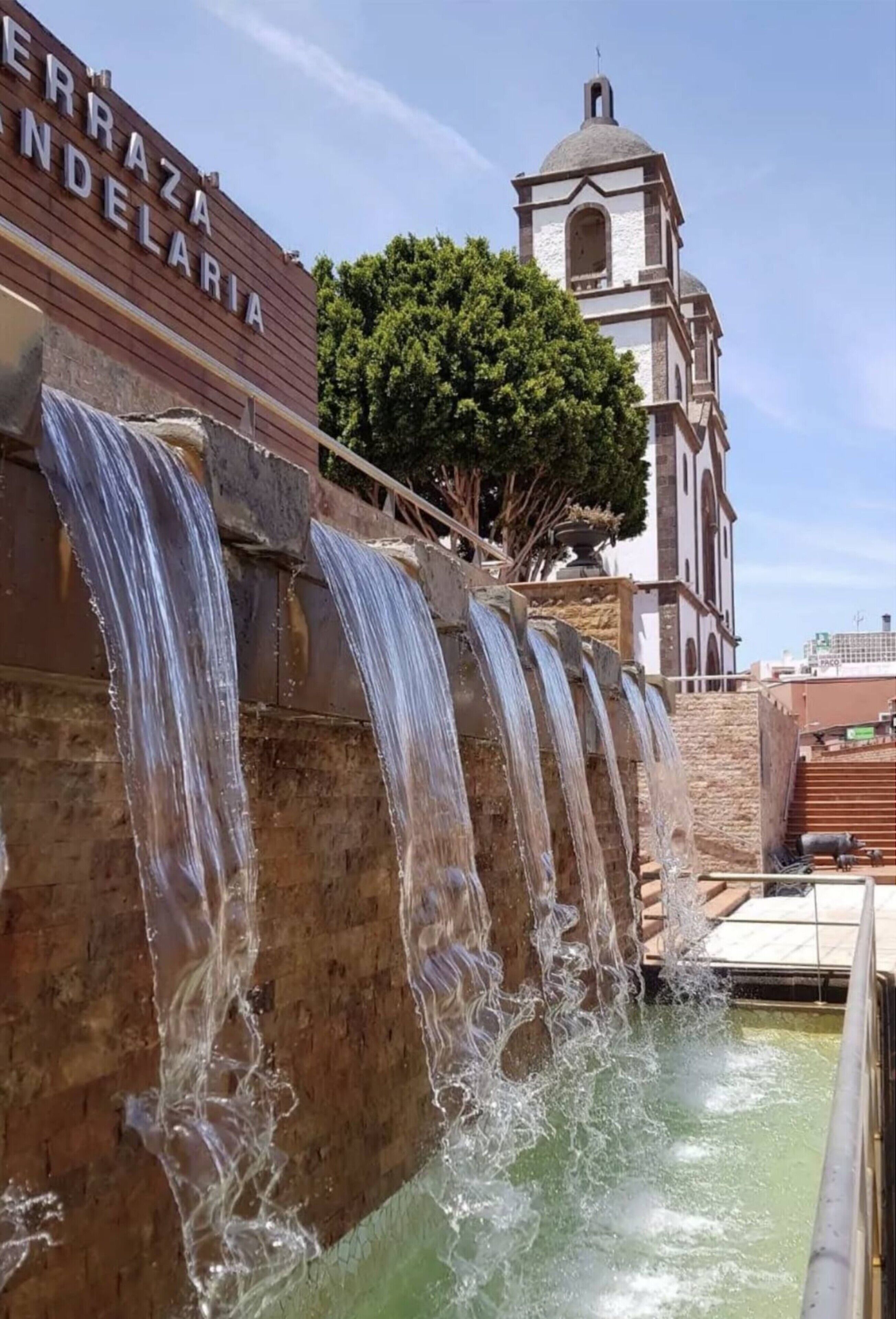 A water feature with multiple cascades, a church tower, and a sign reading 'CERRAZA NDELARIA.'