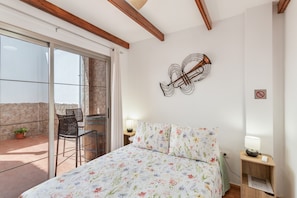 Ein Schlafzimmer mit Bett, Stuhl, Tisch, Lampe und einer Wanddekoration.