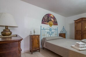 A bedroom with a bed, a nightstand, a lamp, a wooden cabinet, and a wall with a decorative painting.