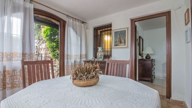A round table with a woven centerpiece, a wooden chair, a white lace tablecloth, a wooden cabinet with a mirror, and a framed picture on the wall.