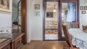 A room with a wooden table, a sofa, a patterned rug, and a door leading to another room.