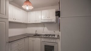 A compact kitchen with white cabinets, a gas stove, an oven, and a single light fixture.
