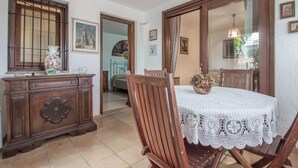 A dining area with a wooden table and chairs, a white lace tablecloth, and a wooden cabinet with decorative items.