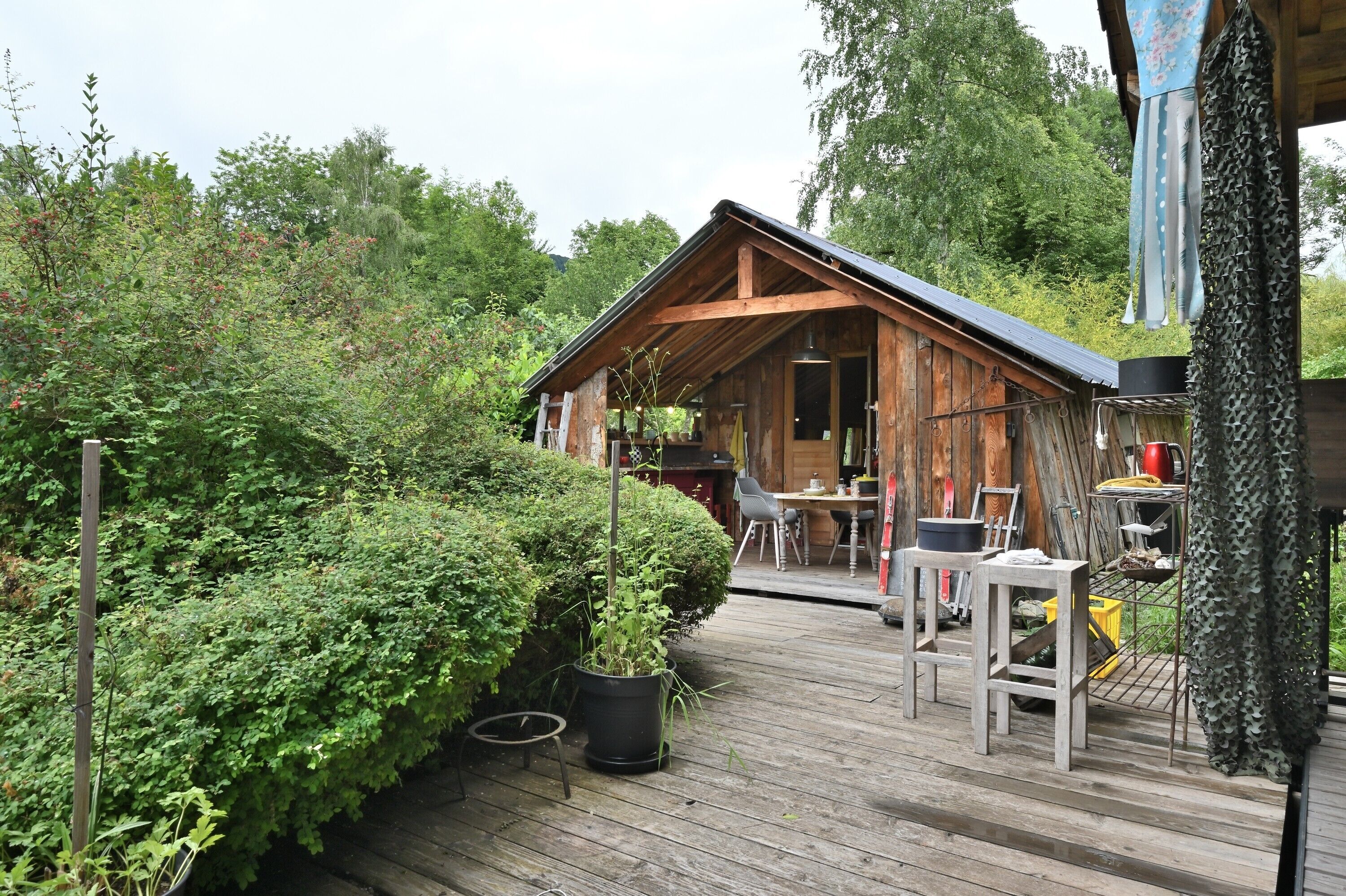 A wooden cabin with a deck, surrounded by dense greenery.