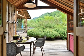 Un terrazzo in legno con tavolo e sedie, vista su dolci colline verdi e interni rustici di una baita.