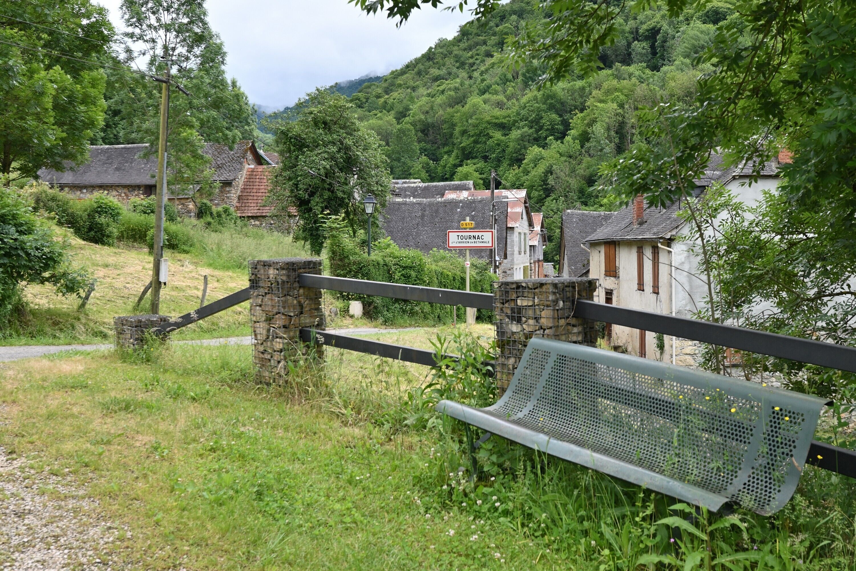 Un borgo rurale con muri in pietra, una panchina e un cartello che indica un'attrazione turistica.