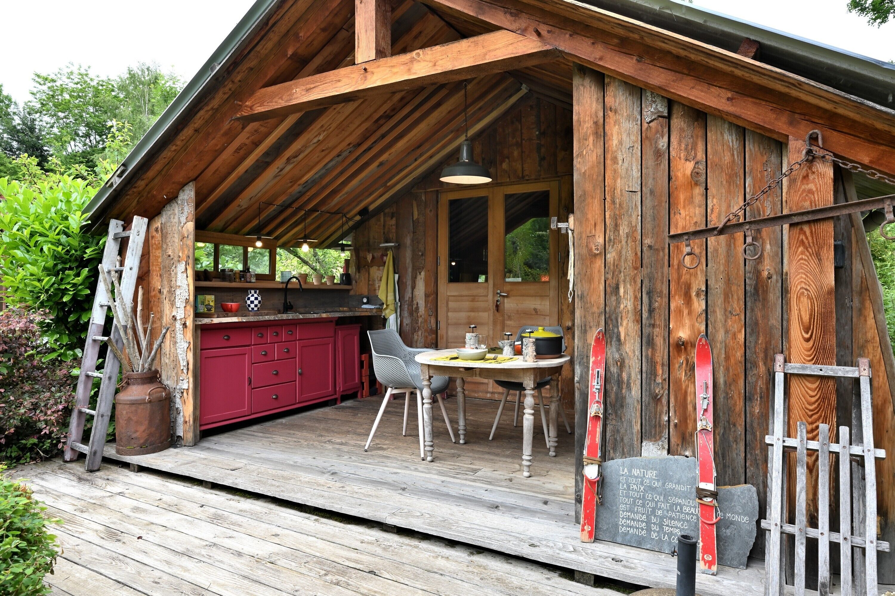 Una cabaña de madera con comedor, cocina roja y terraza de madera.