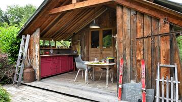 Una cabaña de madera con comedor, cocina roja y terraza de madera.