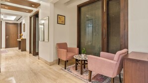 A modern living room with a marble floor, a round coffee table, two pink armchairs, and a wooden cabinet. - Geet by Akama Homes (New Delhi)