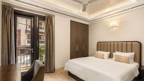 A hotel room with a bed, a desk, a chair, a wardrobe, and a balcony with patterned curtains. - Geet by Akama Homes (New Delhi)