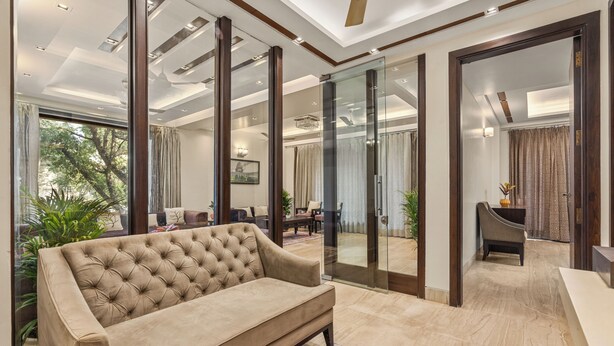 A modern living room with a tufted sofa, large windows, and a view of a mosque. - Geet by Akama Homes (New Delhi)
