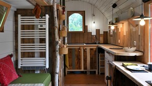 A rustic kitchen with wooden cabinets, a white radiator, and a window with a view of greenery. - Tiny Home 'Roulotte Appoline' with Mountain View, Private Terrace and Garden (Arrien-en-Bethmale)