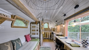 A cabin interior with a wooden ceiling, a dining area, a bench, and a view of the outdoors. - Tiny Home 'Roulotte Appoline' with Mountain View, Private Terrace and Garden (Arrien-en-Bethmale)
