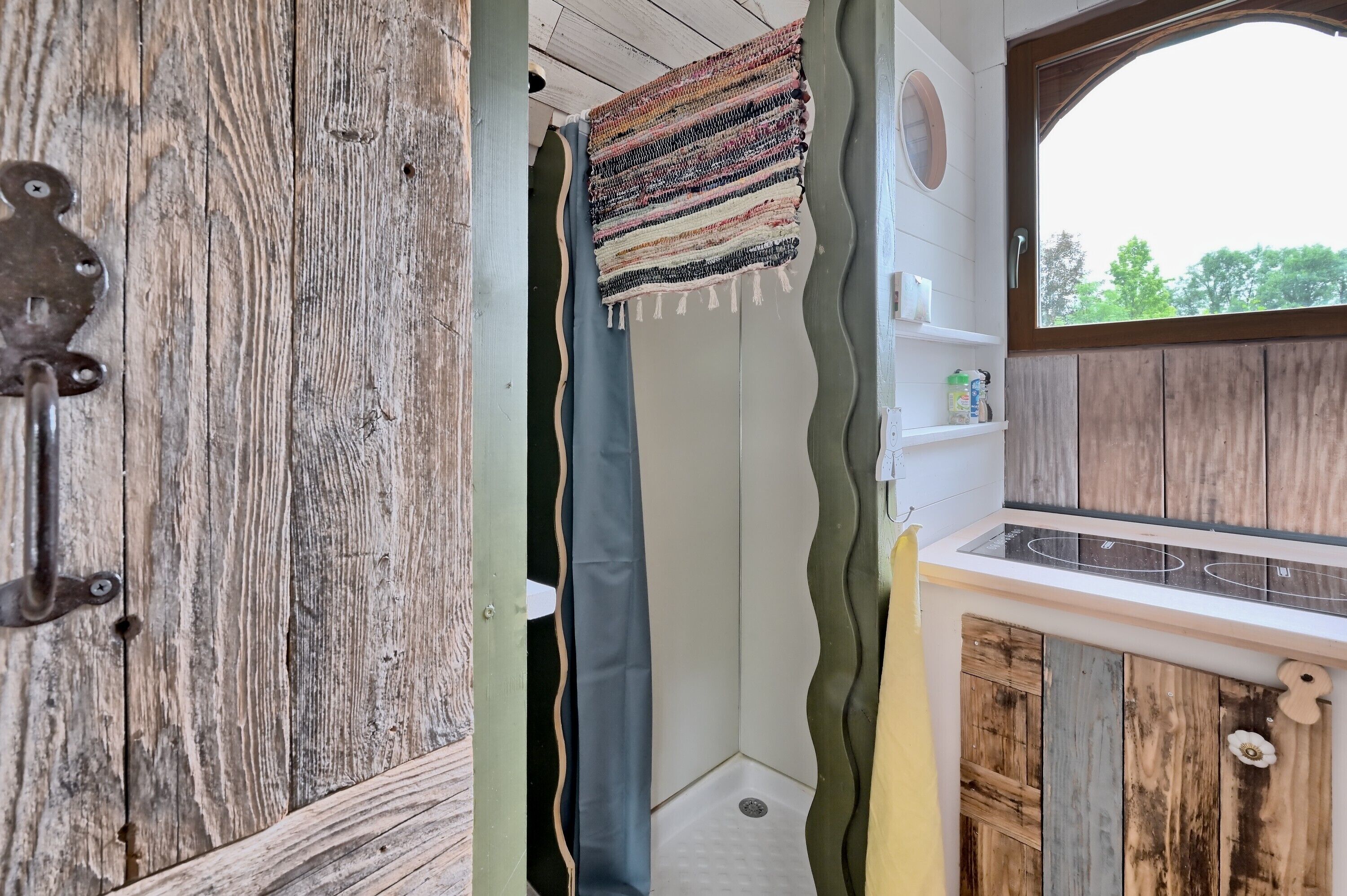 Une salle de bain rustique avec une porte en bois, un rideau de douche et une fenêtre donnant sur les arbres.