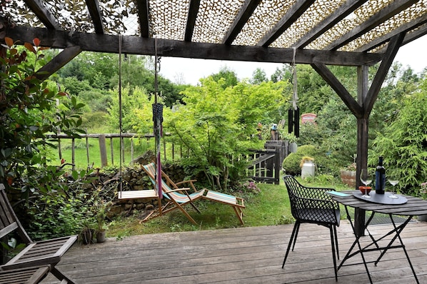 Une terrasse en bois avec une pergola, une balançoire et une table avec des chaises.