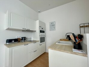 A compact kitchen with white cabinetry, a built-in oven, a coffee maker, and a sink with a wooden countertop.