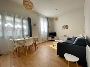 A living room with a sofa, TV, dining table, chairs, and a small white table.