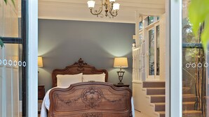 A bedroom with a large bed, a chandelier, and a red carpet leading to the door.