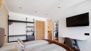 Een moderne slaapkamer met een bed, een bureau, een televisie en inbouwkasten.
