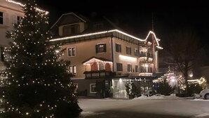 Een hotel met een met sneeuw bedekte grond, een kerstboom met lichtjes en een gebouw met verlichte ramen.