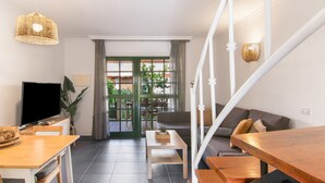 A modern living room with a TV, dining table, sofa, staircase, and a view of the outdoors.