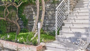 A stone wall, a tree, and a staircase with a metal railing. - The Italian Lady (Alassio)
