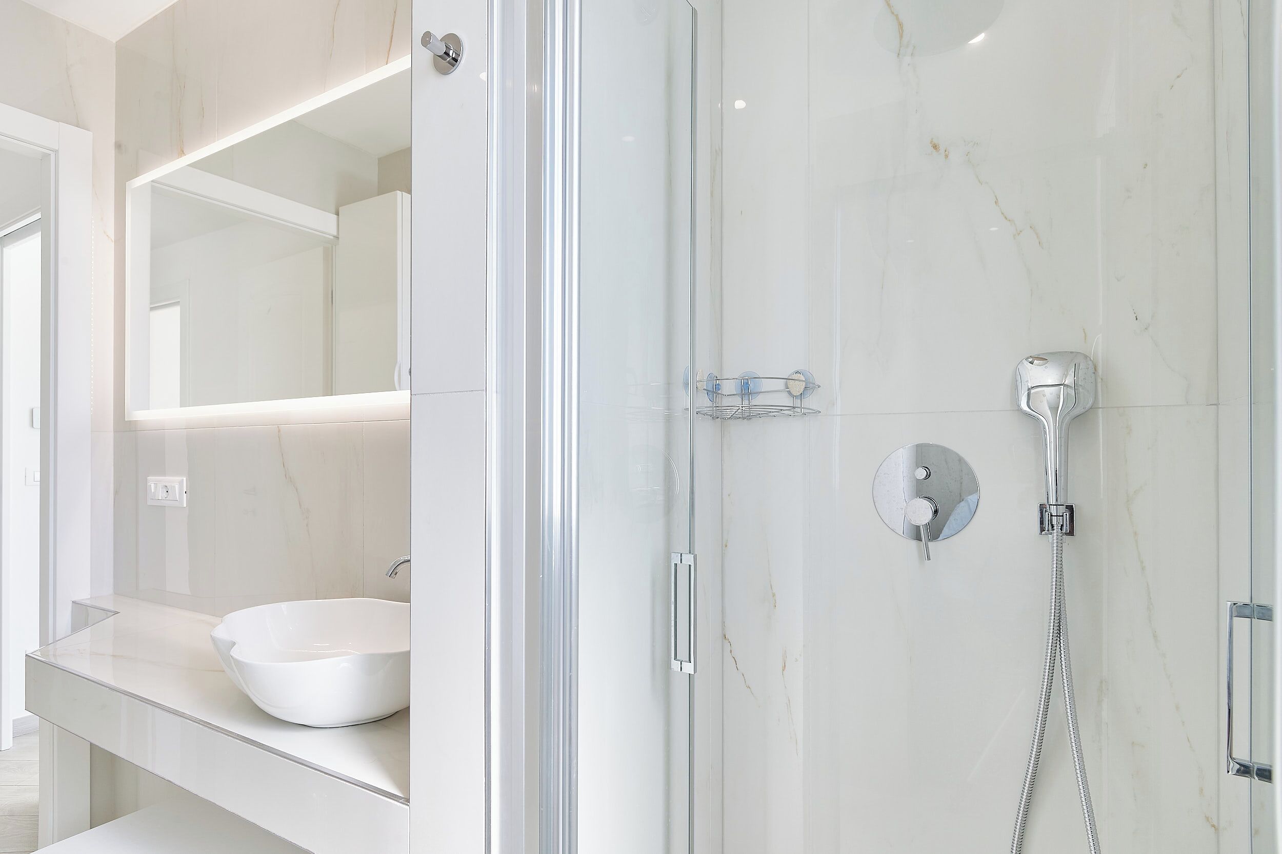 A modern bathroom with a glass-enclosed shower, a white sink, and a large mirror.