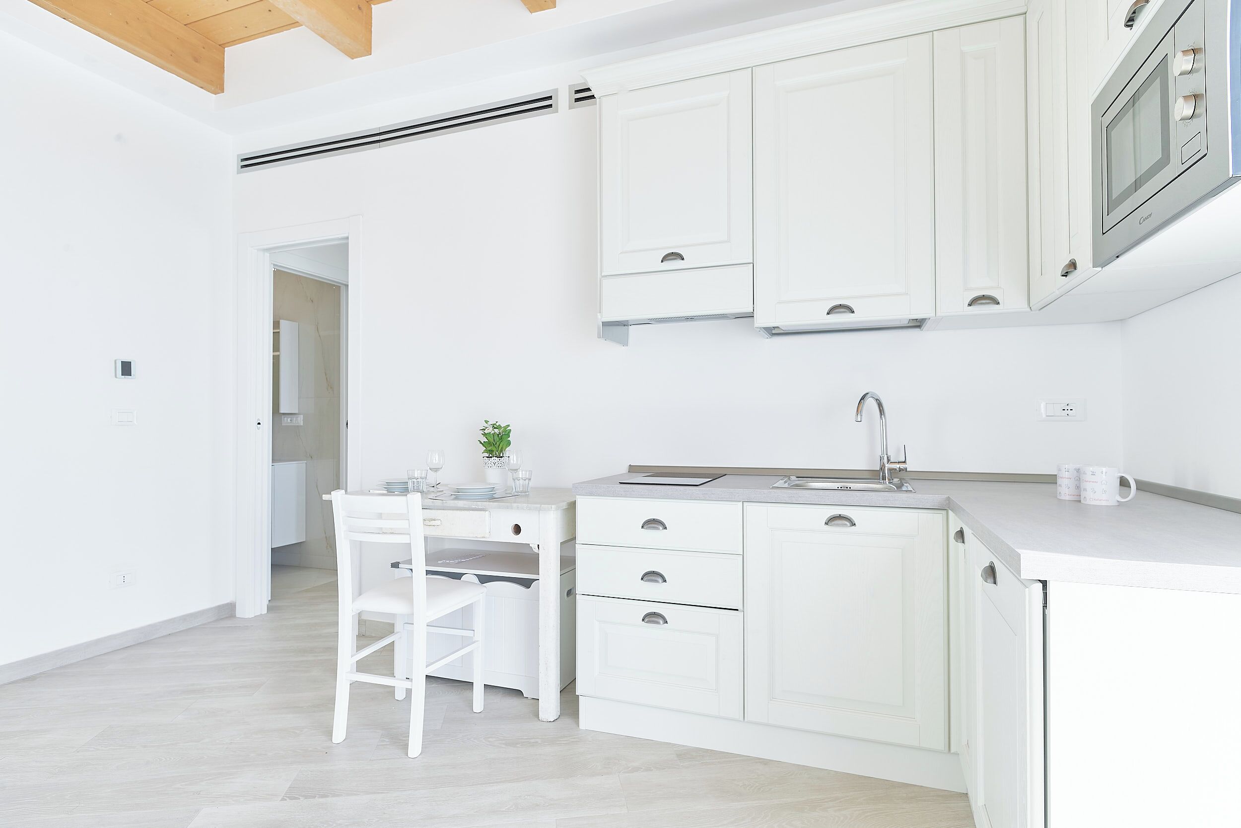 A modern kitchen with white cabinetry, a built-in microwave, and a dining area with a white table and chair.